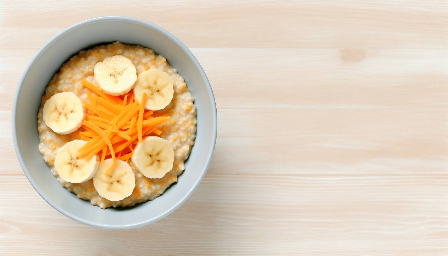 Un tazón de avena cocida decorado con rodajas de plátano y zanahorias ralladas, colocado sobre una...